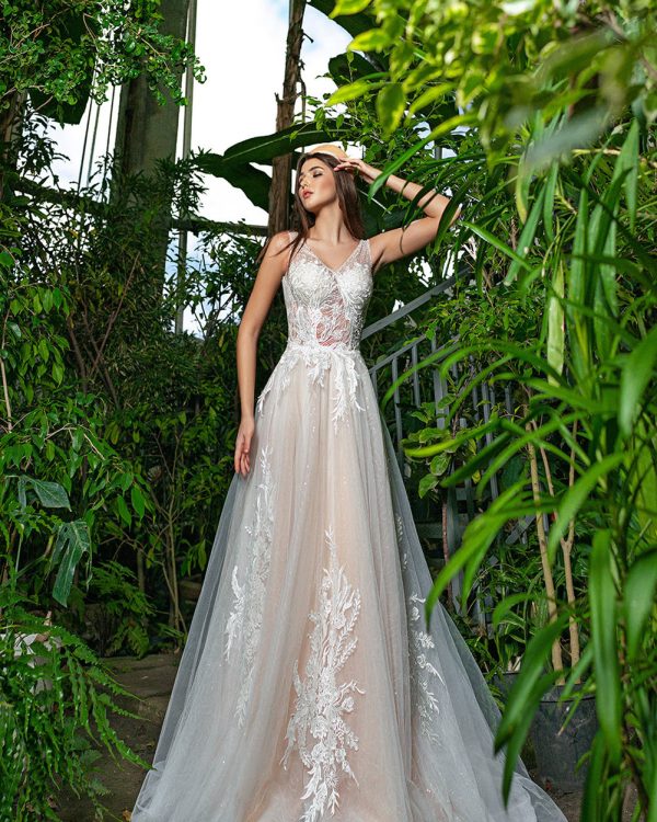 Braut in einem transparenten A-Linien-Brautkleid mit floralen Applikationen und Tüllrock, posierend in einem tropischen Gewächshaus.