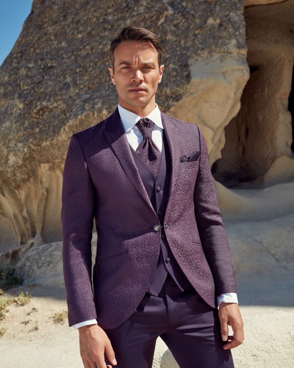 Moderner Hochzeitsanzug in Lila mit Weste, schmalem Revers und Krawatte, getragen vor Felskulisse im Freien