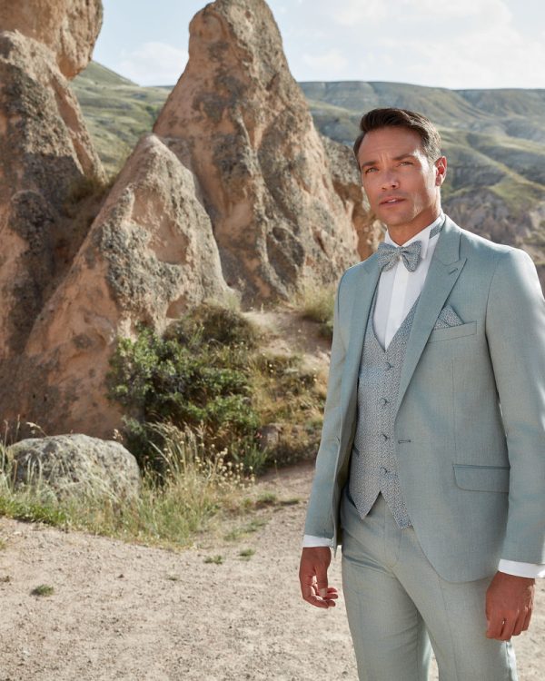 Hellgrüner Hochzeitsanzug für Bräutigam mit Weste und Einstecktuch vor Felslandschaft im Freien