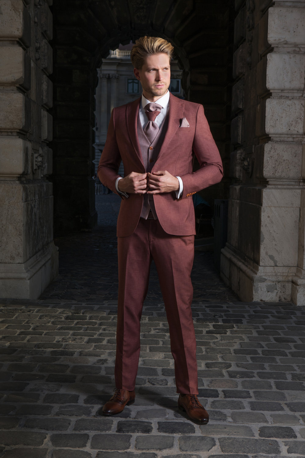 Eleganter Bräutigamanzug in Bordeauxrot mit Weste und Hochzeitskrawatte, getragen in historischer Kulisse mit edlem Flair.