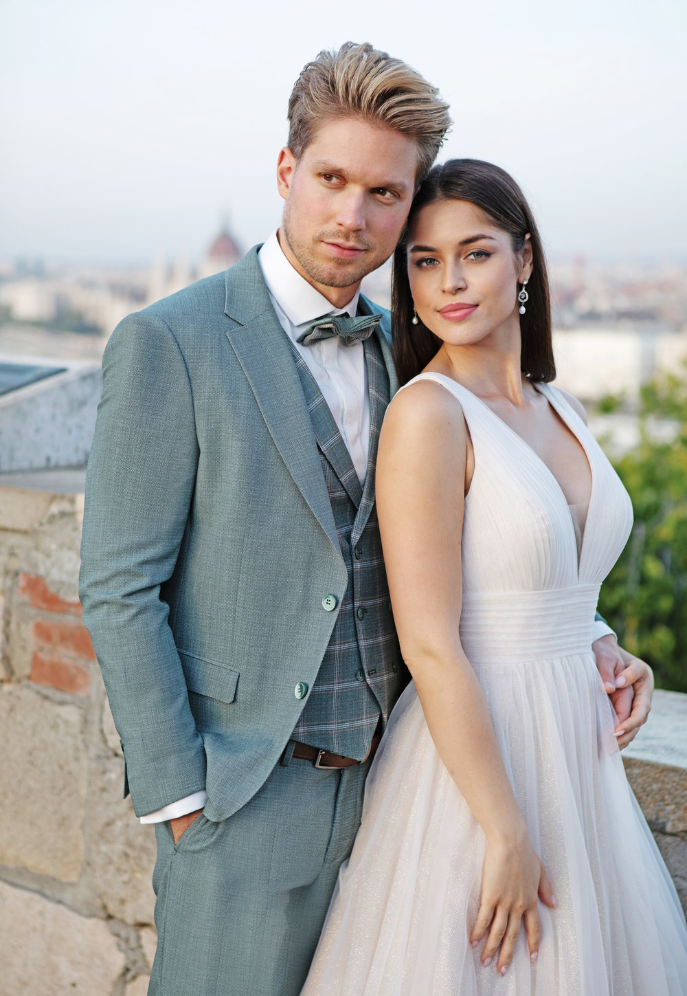 Moderner hellgrüner Bräutigamanzug mit karierter Weste und Fliege – harmonisches Brautpaar-Outfit mit sommerlichem Flair.