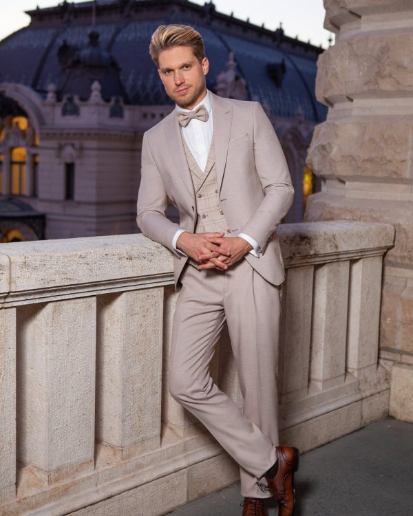 Eleganter, beigefarbener Bräutigamanzug mit Weste und Fliege – stilvoller Hochzeitslook für den modernen Gentleman in romantischer Abendkulisse.