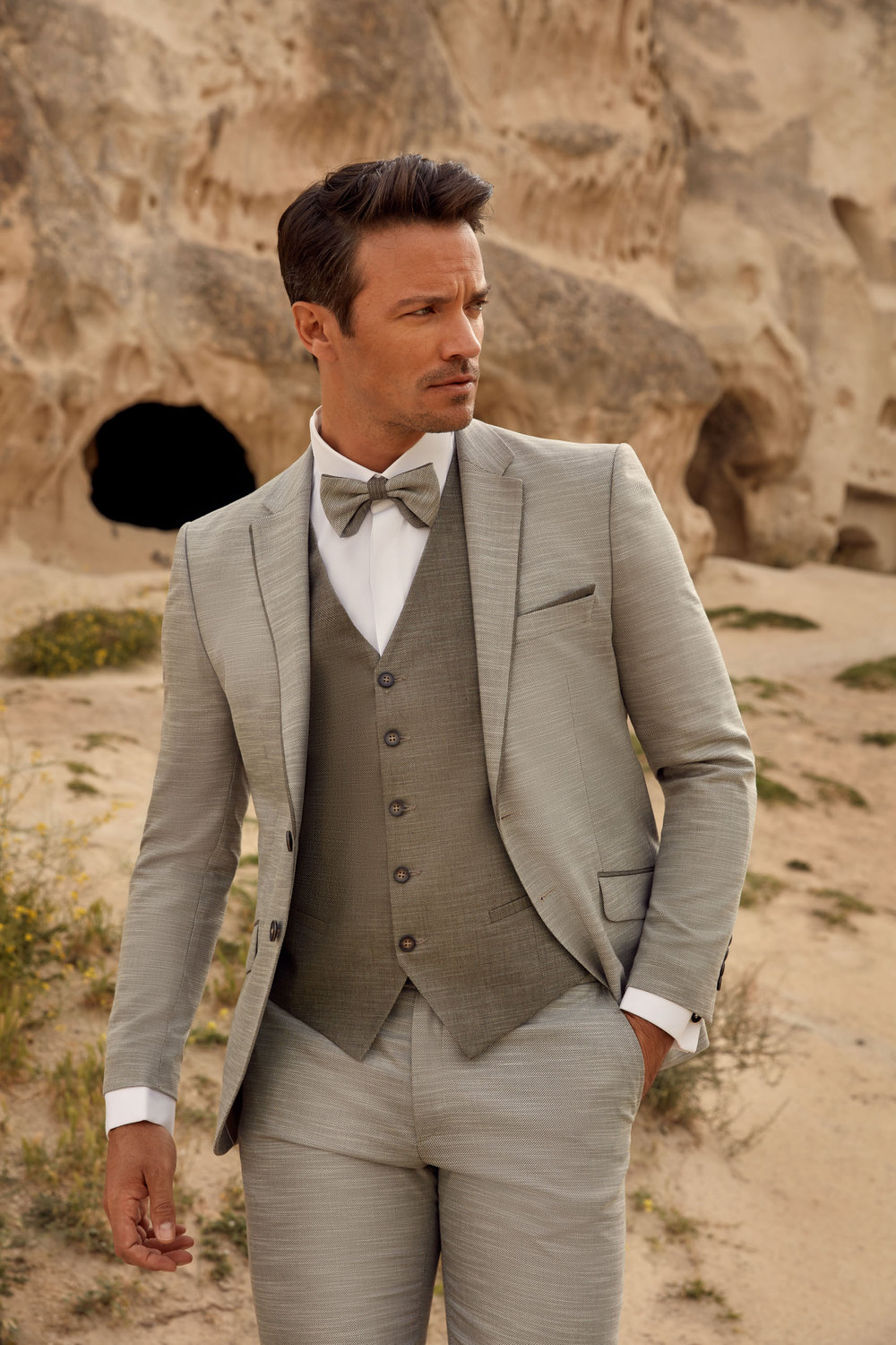 Grauer Bräutigamanzug mit Weste und Fliege – stilvoller Hochzeitslook für moderne Bräutigame in natürlicher Kulisse.