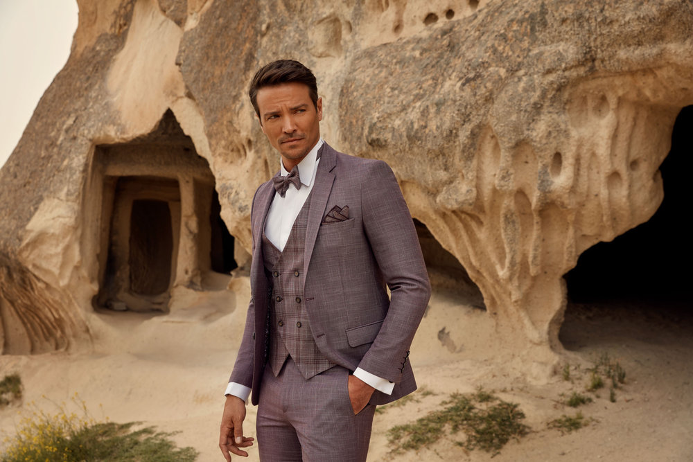 Bordeauxfarbener Bräutigamanzug mit doppelreihiger Weste und Schleife – moderner Hochzeitslook in warmer Naturkulisse.