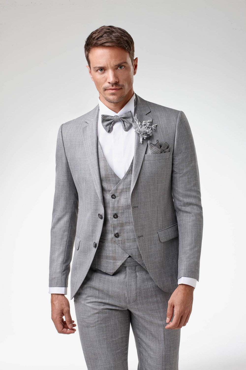 Grauer Bräutigamanzug mit Weste, Fliege und Ansteckblume – eleganter Hochzeitslook für stilbewusste Herren.