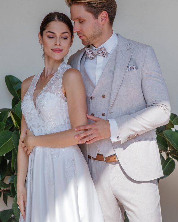Beigefarbener Bräutigamanzug mit gemusterter Fliege und Weste – stilvoller Hochzeitslook im eleganten Paarshooting mit Braut.