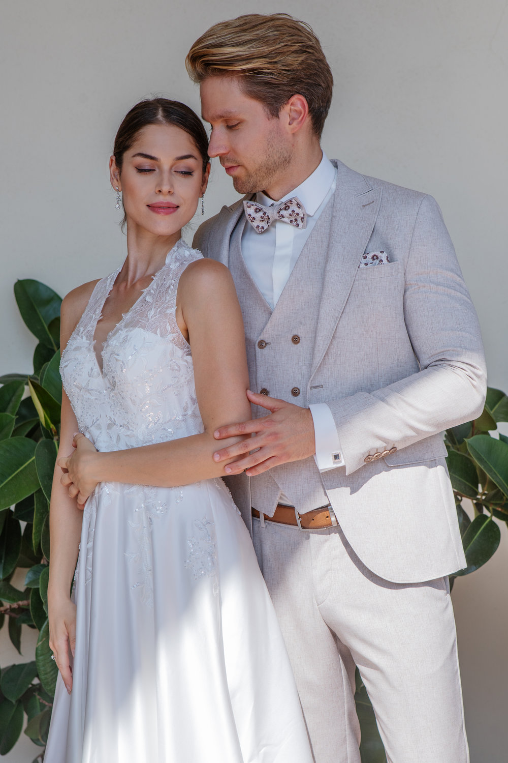 Beigefarbener Bräutigamanzug mit gemusterter Fliege und Weste – stilvoller Hochzeitslook im eleganten Paarshooting mit Braut.