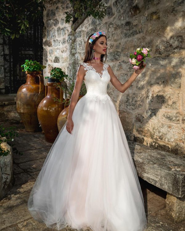 Prinzessinnen-Brautkleid mit Tüllrock, tiefem Tattoo-Rückenausschnitt und Knopfleiste, romantische Kulisse mit Blumenkranz.