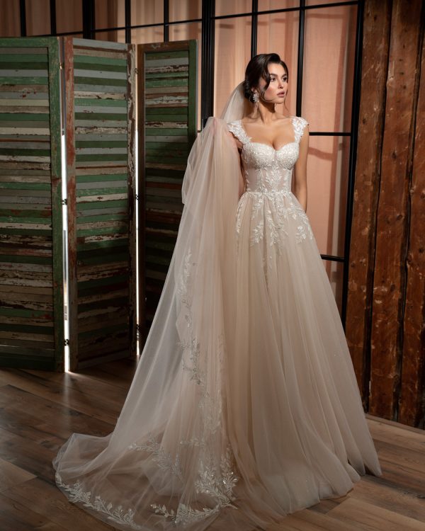 Romantisches, glitzerndes Brautkleid mit Schleppe, transparenter Corsage und Tüllärmeln in einem eleganten Innenraum, aufgenommen im Abendlicht.