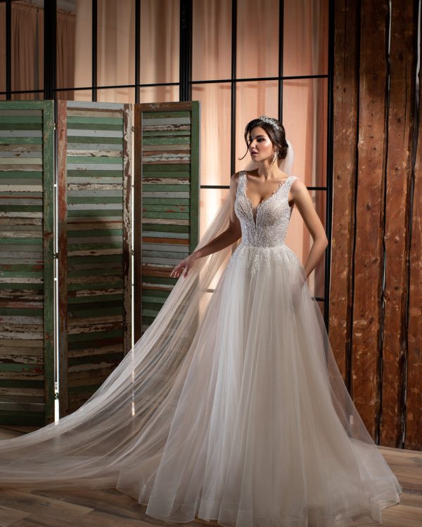 Elegantes Prinzessin-Brautkleid mit tiefem Ausschnitt und glitzerndem Tüllrock, fotografiert in rustikalem Innenraum mit Vintage-Holzelementen.
