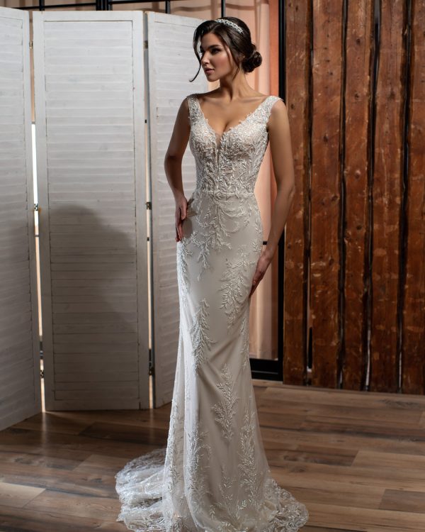 Elegantes Fit & Flare Brautkleid mit tiefem V-Ausschnitt, glitzernder Spitze und langer Schleppe – aufgenommen in stilvoller Indoor-Kulisse mit rustikaler Holzwand.