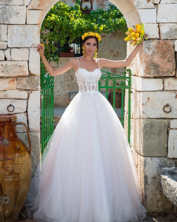 Prinzessinnen-Brautkleid mit Schnürung und Tüllrock, romantische Aufnahme vor einem Steinbogen mit floralen Akzenten.