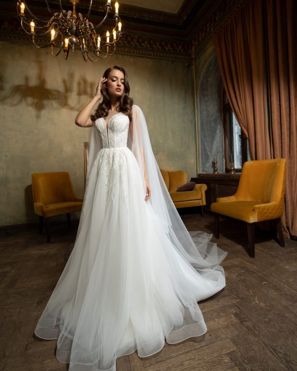 Elegantes Prinzessin Brautkleid mit fließendem Rock, transparenter Corsage und romantischen Cape-Ärmeln – fotografiert in einem stilvollen Vintage-Ambiente mit Kronleuchter.