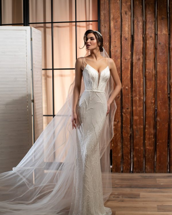 Modernes Fit & Flare Brautkleid mit schmalem Schnitt, tiefem V-Ausschnitt und Spaghettiträgern – aufgenommen im eleganten Loft-Ambiente mit langem Schleier.