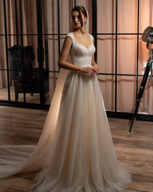 Prinzessinnen-Brautkleid mit zartem Glitzertüllrock, besticktem Oberteil und eleganter Knopfleiste – aufgenommen in einem stilvollen Loft mit Holzboden und Studio-Ambiente.