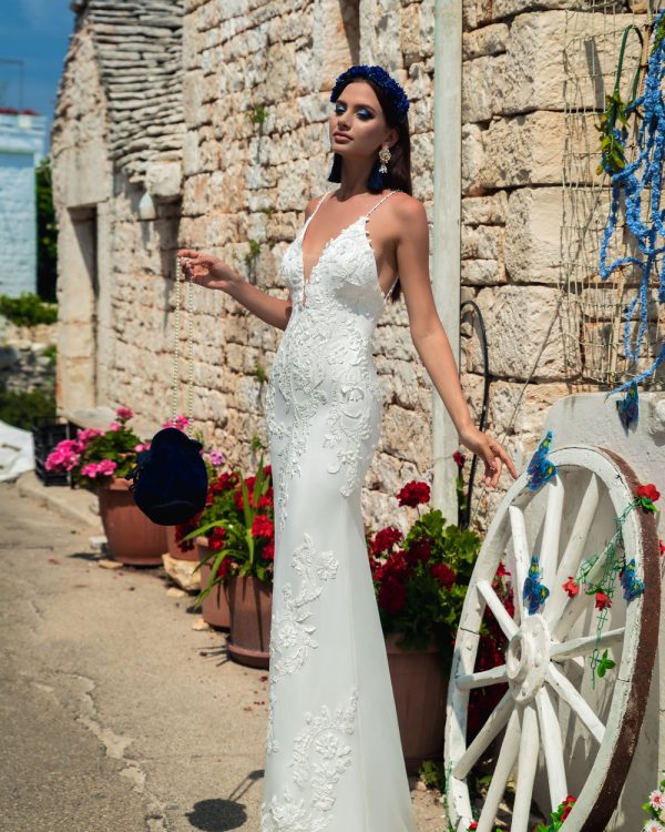 Fit & Flare Brautkleid mit Spitze, tiefem Rückenausschnitt und figurbetontem Schnitt – sommerliche Kulisse mit Steinwand.