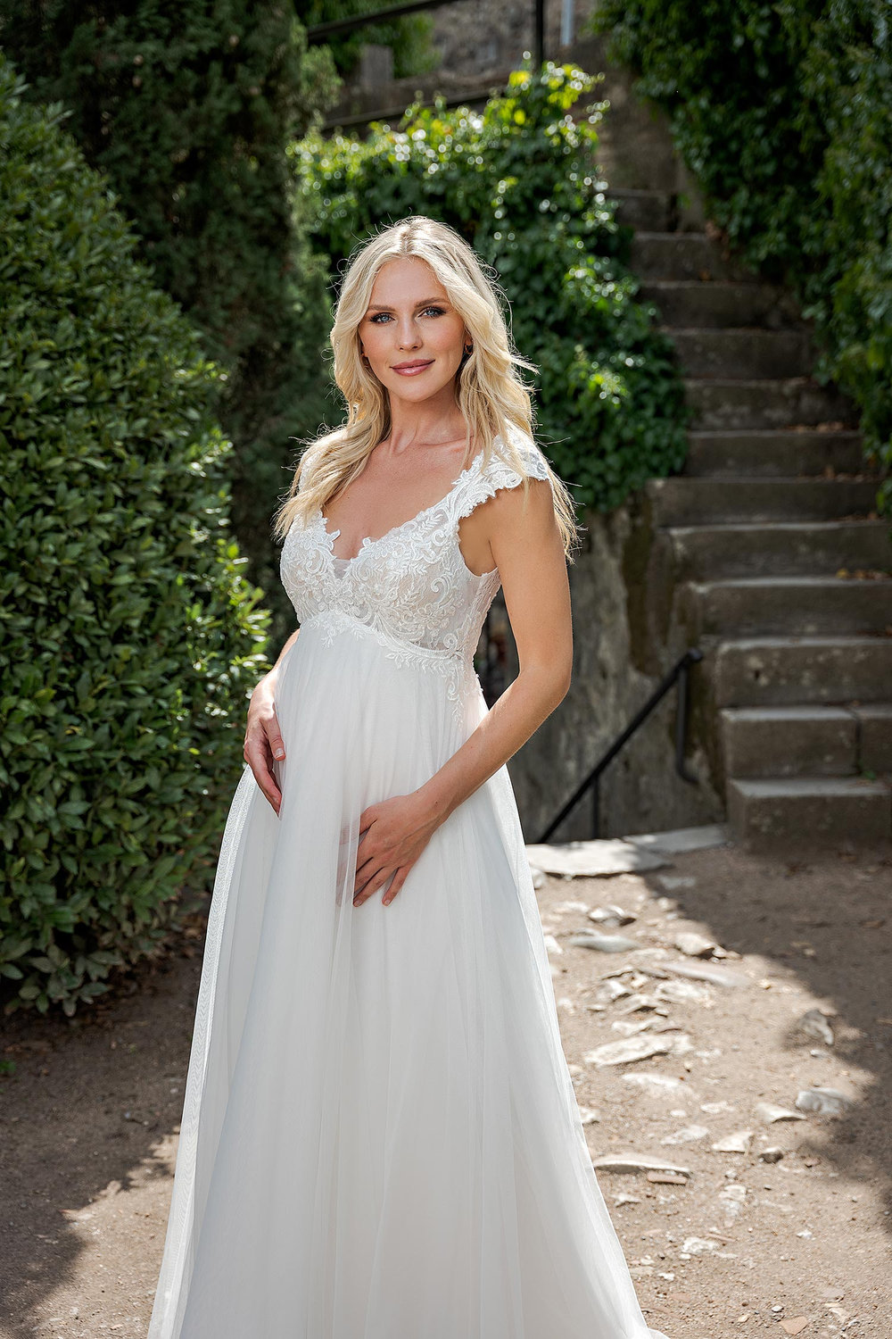 Detailaufnahme vom Spitzenoberteil eines eleganten Umstandsbrautkleides in Gartenumgebung