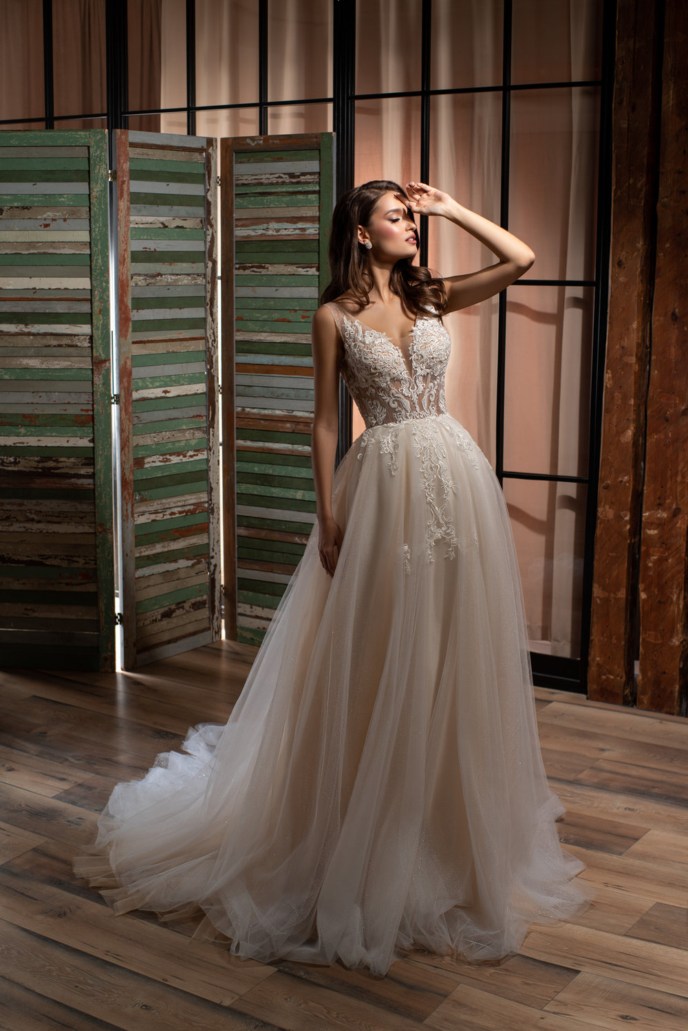 Prinzessin Brautkleid mit tiefem V-Ausschnitt und floral besticktem Spitzenoberteil, Tüllrock in fließender A-Linie, fotografiert vor rustikalem Holzdekor.