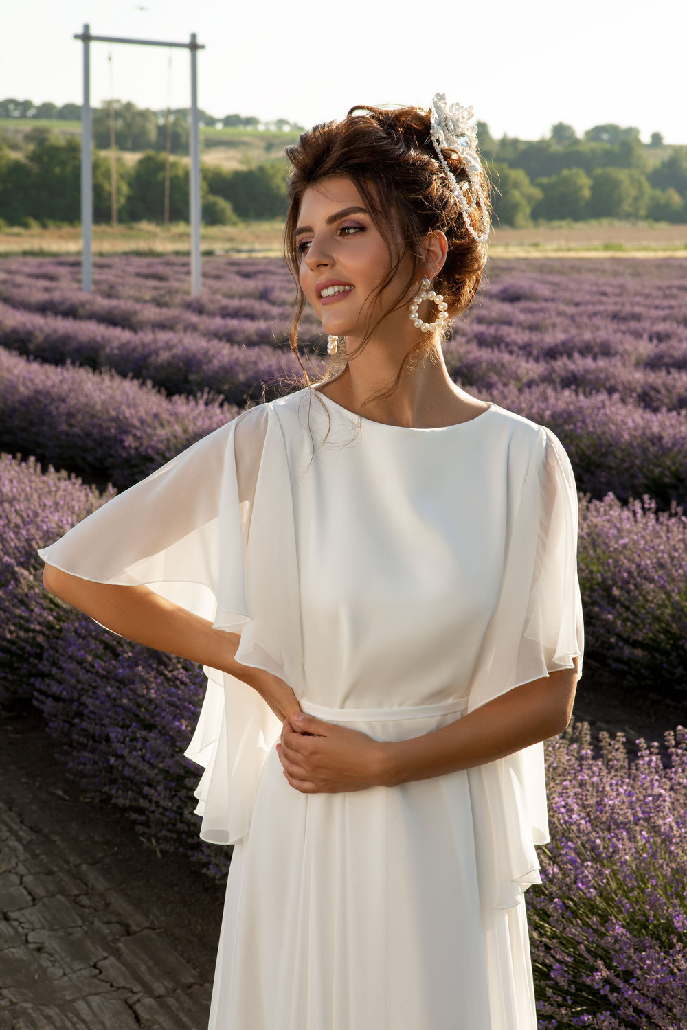 Nahaufnahme eines Chiffon-Brautkleides mit fließendem Schnitt und lockeren Flügelärmeln, fotografiert im Lavendelfeld.