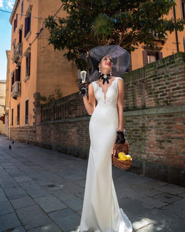 Fit & Flare Brautkleid mit Spitze, Reißverschluss und tiefem Rückenausschnitt – elegante Braut posiert auf mediterraner Straße mit sommerlichen Accessoires.