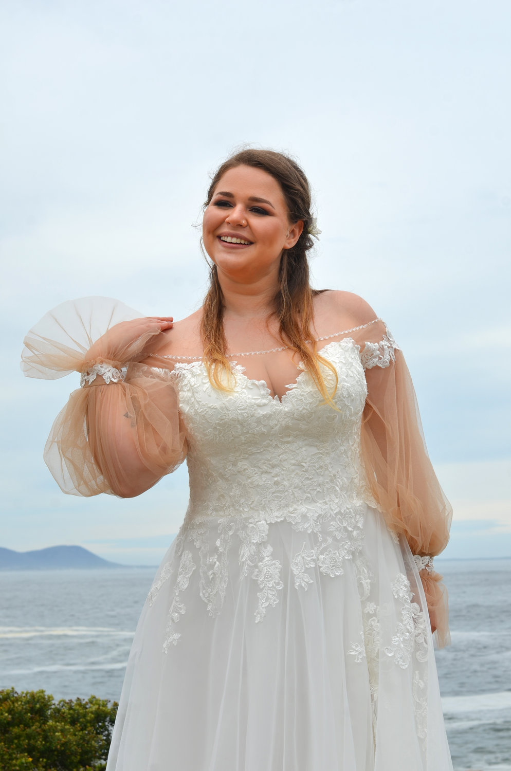 Detailaufnahme eines modernen Curvy Brautkleids mit Herz-Ausschnitt, zarter Spitze und langen Tüllärmeln mit Perlenmanschette.