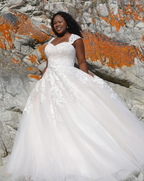 Curvy Braut in weißem Brautkleid mit romantischer Spitze, Herzausschnitt und ausgestelltem Tüllrock vor Felswand mit orangefarbenem Moos.