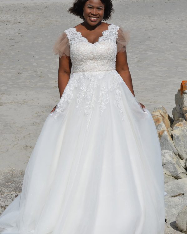 Curvy Braut in romantischem Brautkleid mit Spitzenoberteil und ausgestelltem Tüllrock am Strand.
